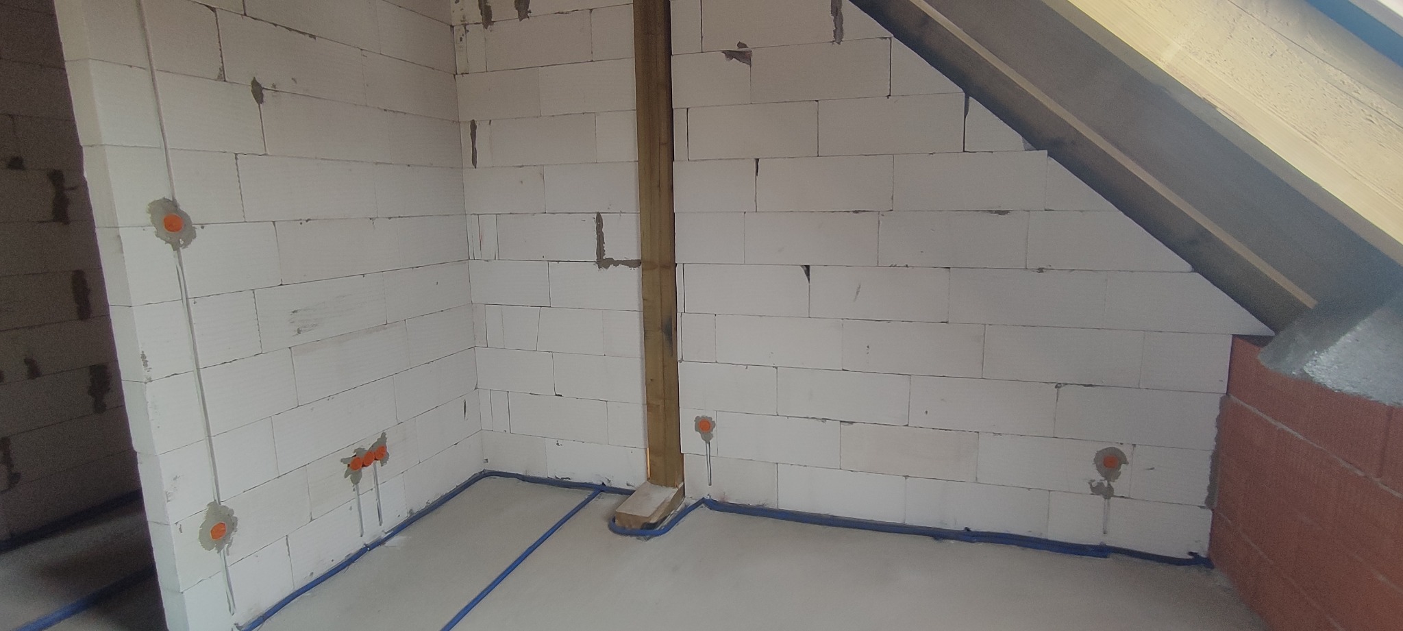 Surowy stan poddasza z instalacją elektryczną w peszlach, widoczne puszki podtynkowe i ściany z betonu komórkowego, przygotowane do dalszych prac wykończeniowych.