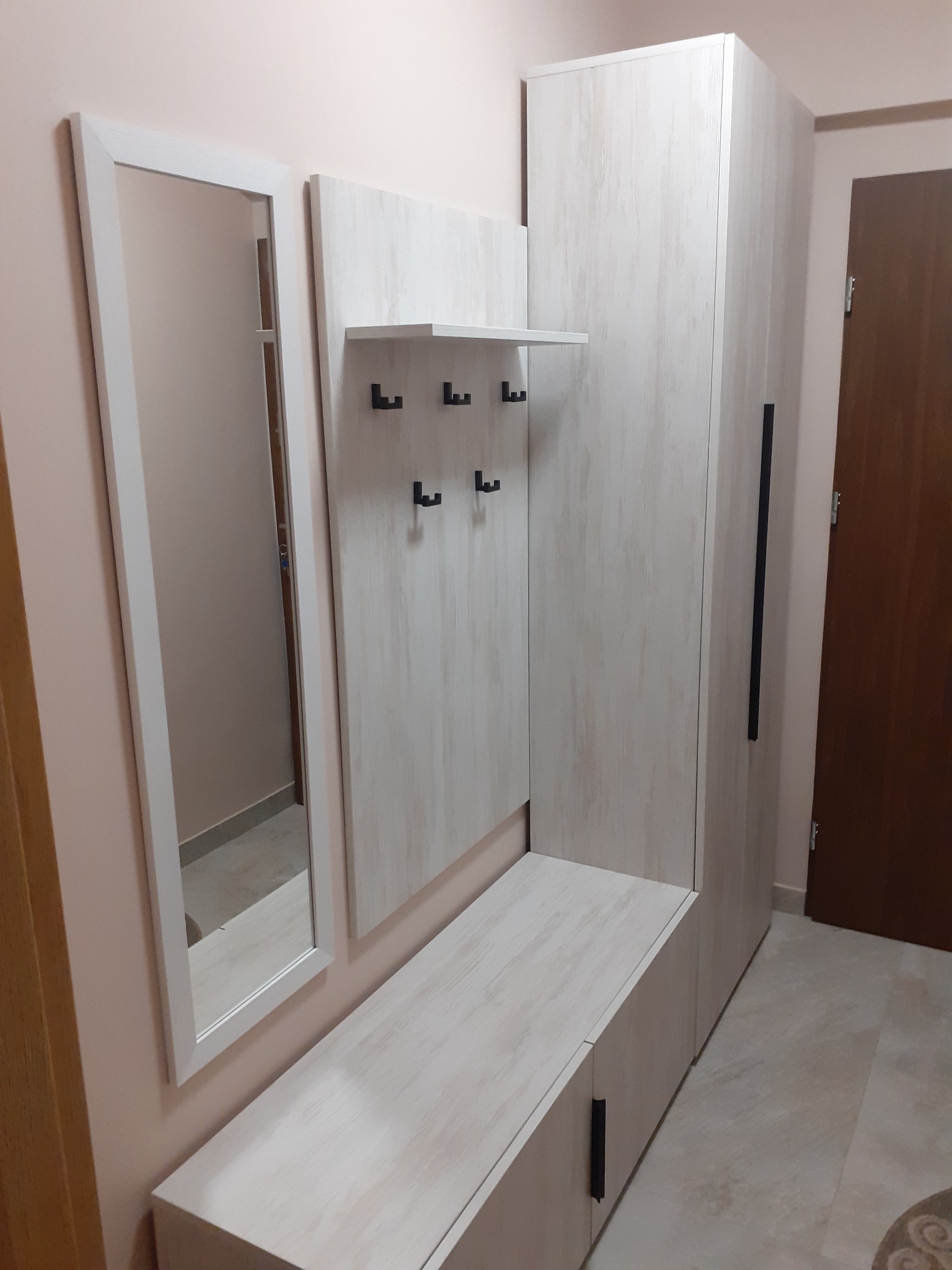 Komplet mebli do przedpokoju w odcieniach bieli i beżu: szafa z długim uchwytem, siedzisko z szafką, panel z wieszakami i lustro w białej ramie.