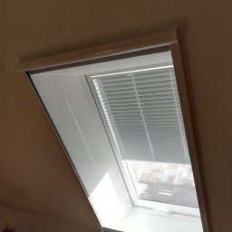 F.H.U. Artur Grabarczyk - Okno dachowe z zamontowaną moskitierą i częściowo opuszczonymi żaluzjami aluminiowymi, widok na zewnątrz.