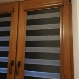 Drewniane okno z zamontowaną roletą dzień noc w kolorze szaro-czarnym, widoczny mechanizm sterujący roletą po prawej stronie.