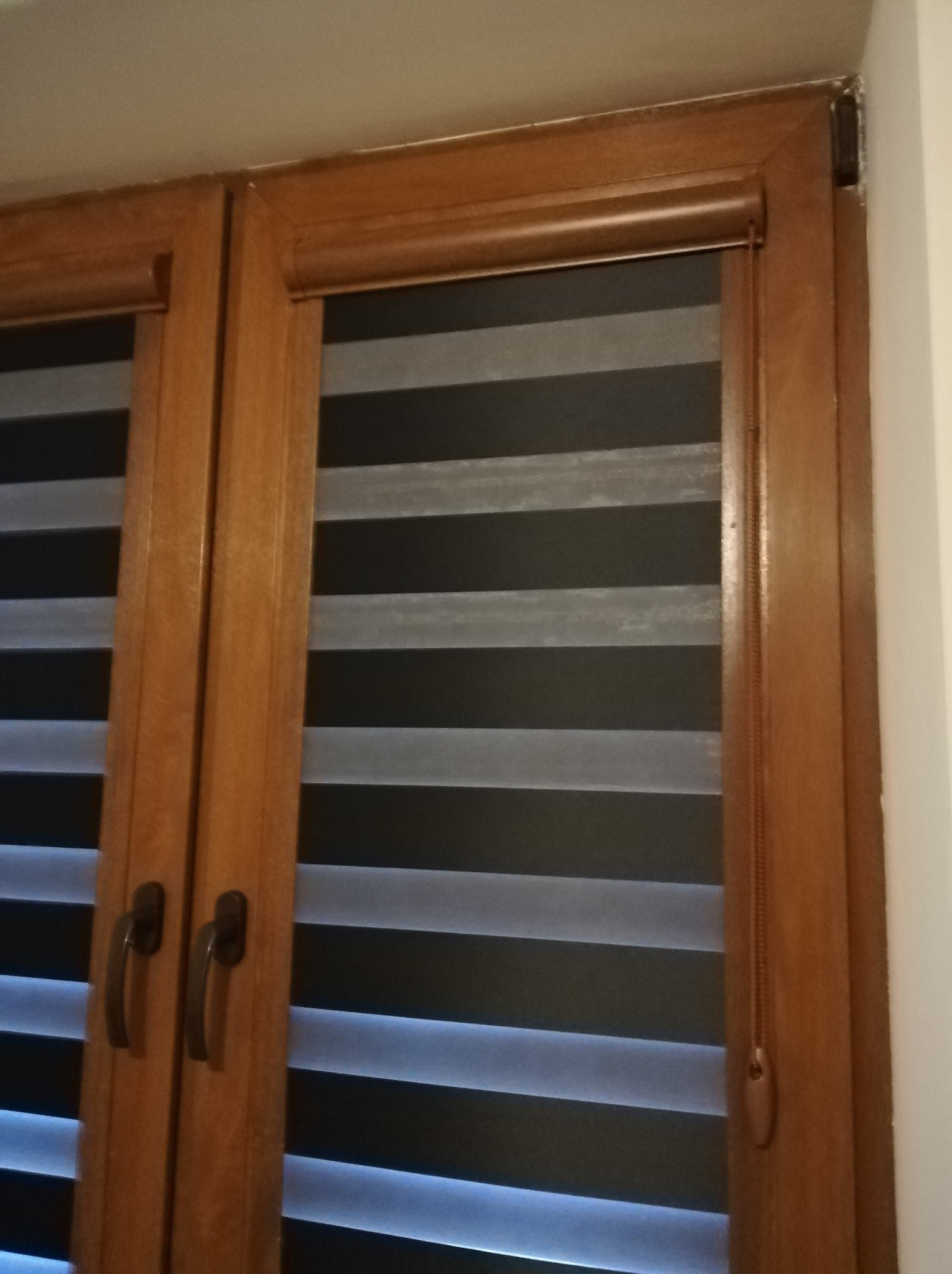 Drewniane okno z zamontowaną roletą dzień noc w kolorze szaro-czarnym, widoczny mechanizm sterujący roletą po prawej stronie.