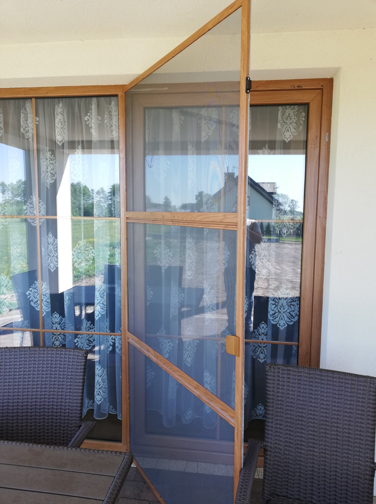 Otwarta moskitiera ramkowa z drewnianym profilem, widok z tarasu na zewnątrz, przezroczysta siatka zabezpiecza przed owadami.