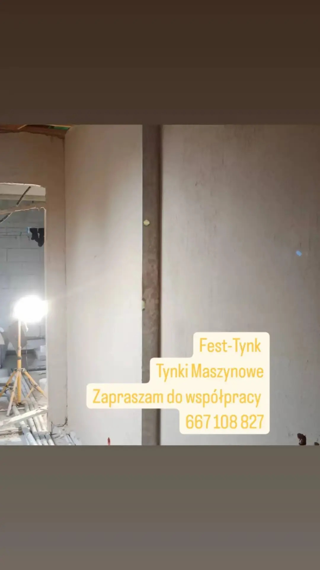 Świeżo nałożony tynk maszynowy na ścianie wewnętrznej, widoczny fragment oświetlenia budowlanego i konstrukcja sufitu w trakcie prac wykończeniowych.