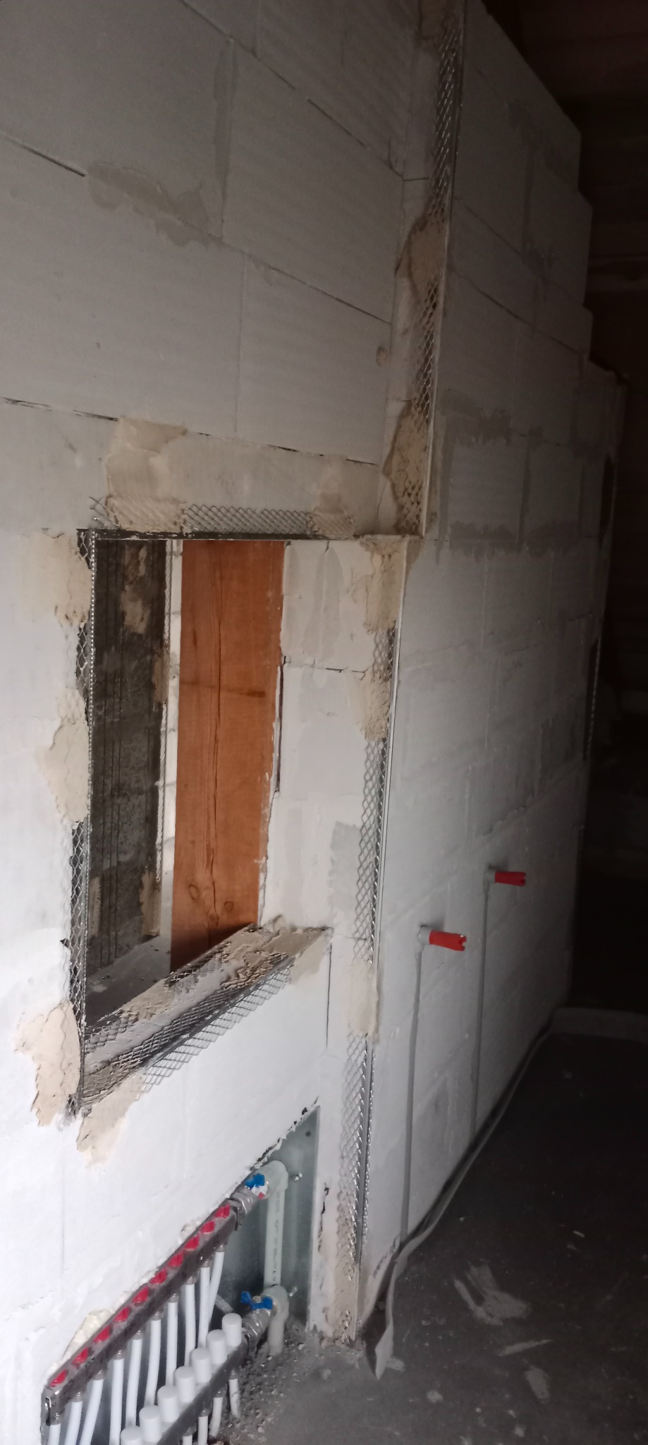 Przygotowanie ściany z gazobetonu pod tynkowanie: zamontowana siatka wzmacniająca na narożnikach i wokół otworu okiennego, widoczna instalacja ogrzewania podłogowego w dolnej części ściany.