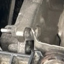 Mobilny Mechanik Elektryk Samochodowy Gdańsk Gdynia Sopot - Szczegółowy widok na brudny, metalowy element mechaniczny w komorze silnika samochodowego, z widocznymi przewodami i śrubami.