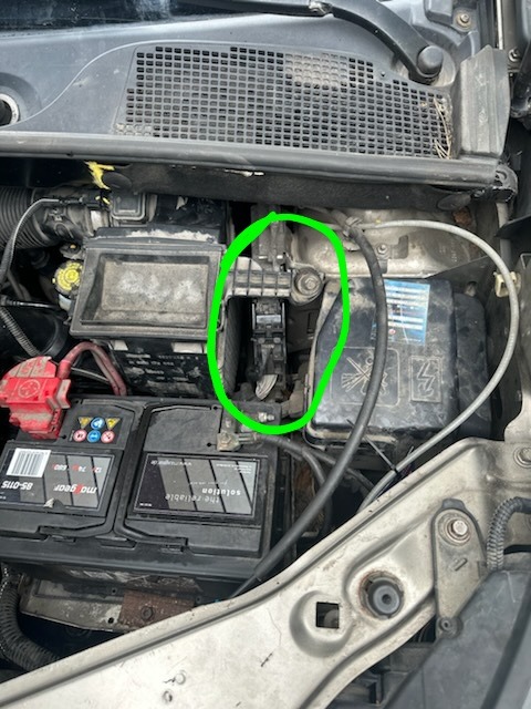 Widok z góry na brudny silnik samochodu z widocznym akumulatorem i filtrem powietrza, z zaznaczonym na zielono obszarem potencjalnej usterki.