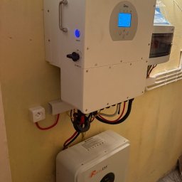 Karol Szczęsny - Zamontowany biały falownik Deye i bateria Felicity ESS na żółtej ścianie. Widoczne kable i elementy instalacji.
