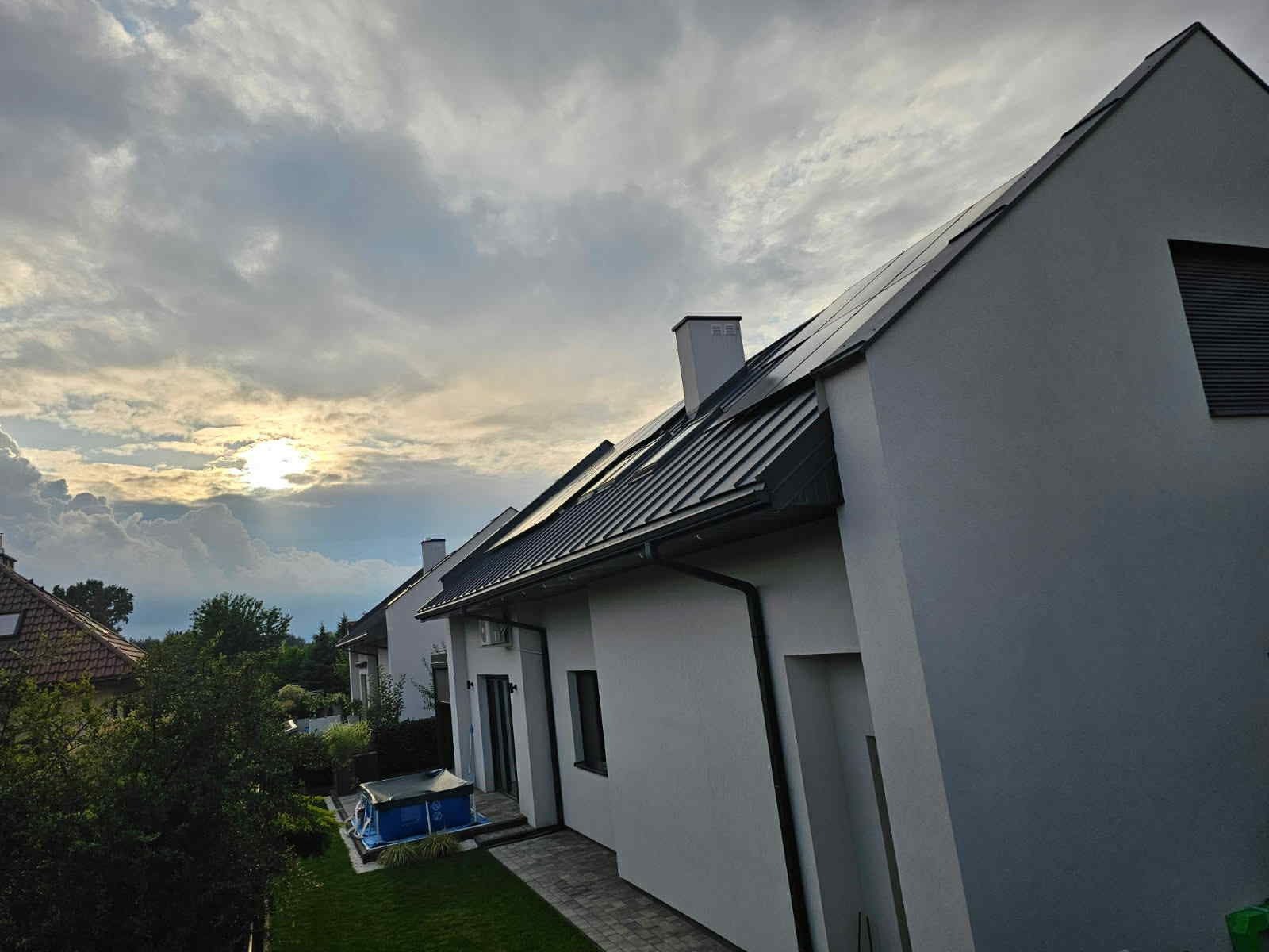 Panele słoneczne na dachu domu jednorodzinnego w Rzeszowie, widok z boku, zachmurzone niebo w tle. Instalacja fotowoltaiczna na ukończonym budynku.