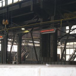 Radiator - Wnętrze hali przemysłowej z widoczną suwnicą, stalowymi konstrukcjami, oknami i grzejnikami przemysłowymi.