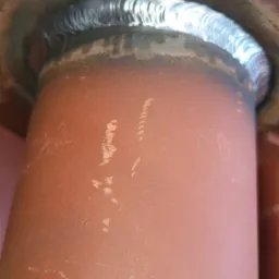 Spoina spawalnicza łącząca rurę z kołnierzem, widoczne ślady po spawaniu na pomarańczowej powierzchni.