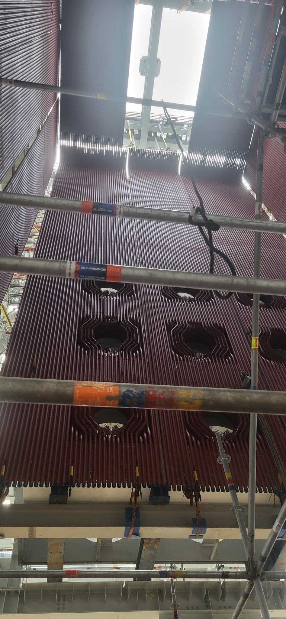 Wnętrze kotła przemysłowego z rurami wodnymi, widok z dołu na rusztowanie, z otworami inspekcyjnymi i mocowaniami.