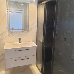 Letex - Nowoczesna łazienka z biało-czarnymi marmurowymi płytkami, białą szafką pod umywalką z czarnymi uchwytami, lustrem z podświetleniem LED i czarną kabiną prysznicową z deszczownicą.