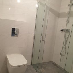 Letex - Nowoczesna łazienka z białymi marmurkowymi płytkami, podwieszaną toaletą i kabiną prysznicową ze szklanymi drzwiami, widok z boku.