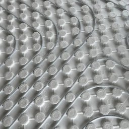 MAZUR SERVICE SPÓŁKA Z OGRANICZONĄ ODPOWIEDZIALNOŚCIĄ - Szare rurki ogrzewania podłogowego ułożone na białej izolacji z wypustkami, widok z góry pod kątem.