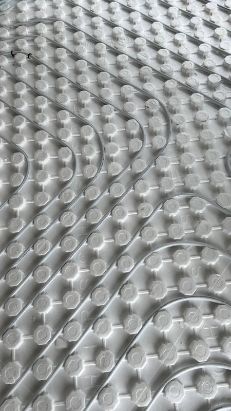 Szare rurki ogrzewania podłogowego ułożone na białej izolacji z wypustkami, widok z góry pod kątem.