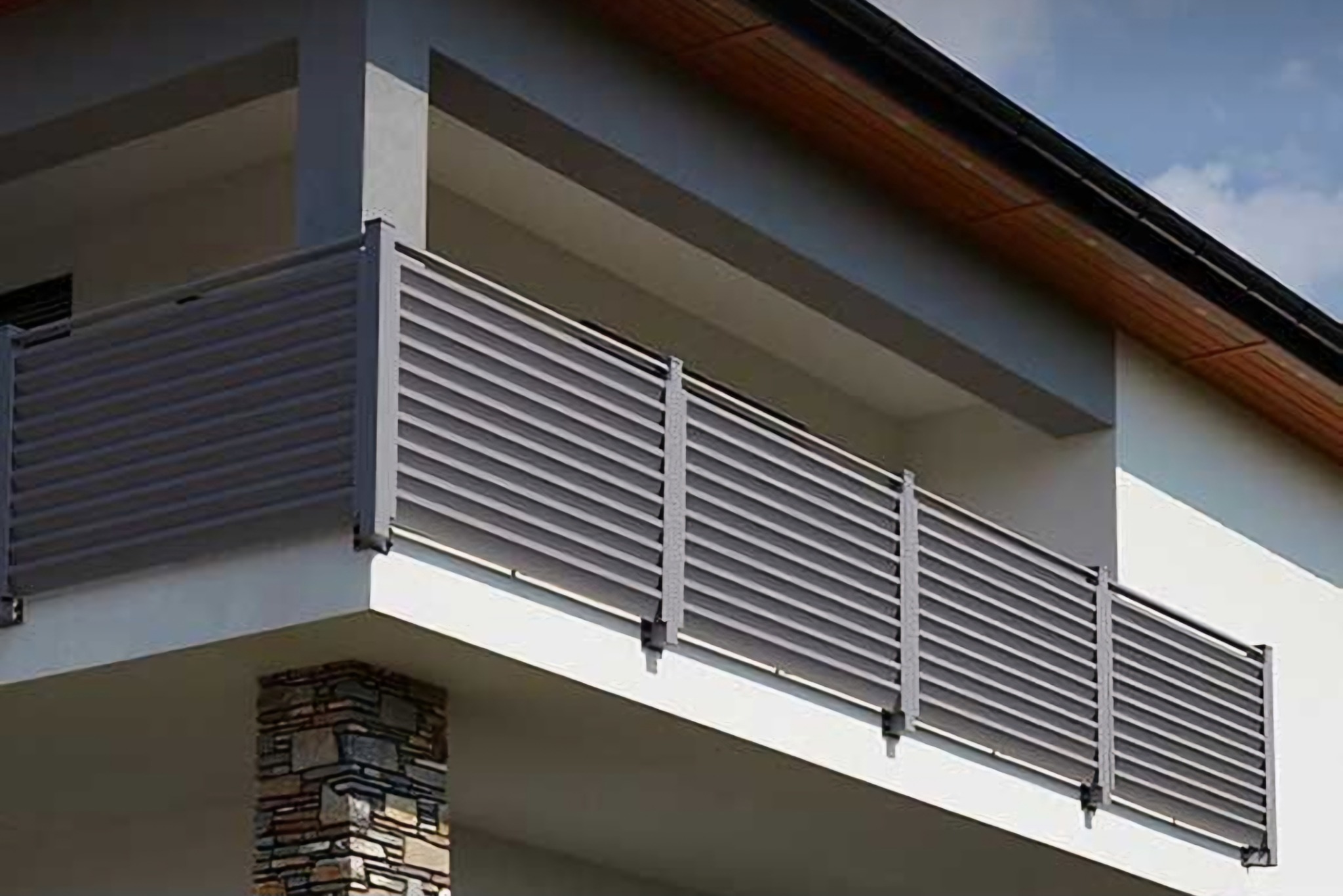 Nowoczesna balustrada balkonowa z poziomych, grafitowych paneli, zamontowana na białym budynku z kamienną kolumną.