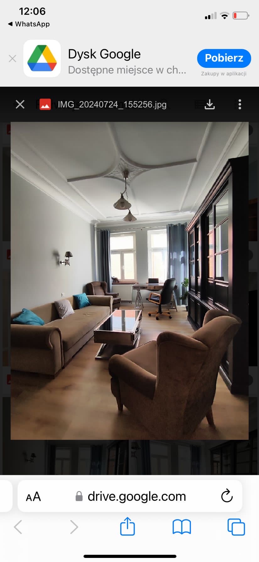 Jasne wnętrze pokoju dziennego z kremową sofą, fotelami, czarnym regałem i dwoma oknami z szarymi zasłonami; widoczny ozdobny sufit z listwami i lampami.