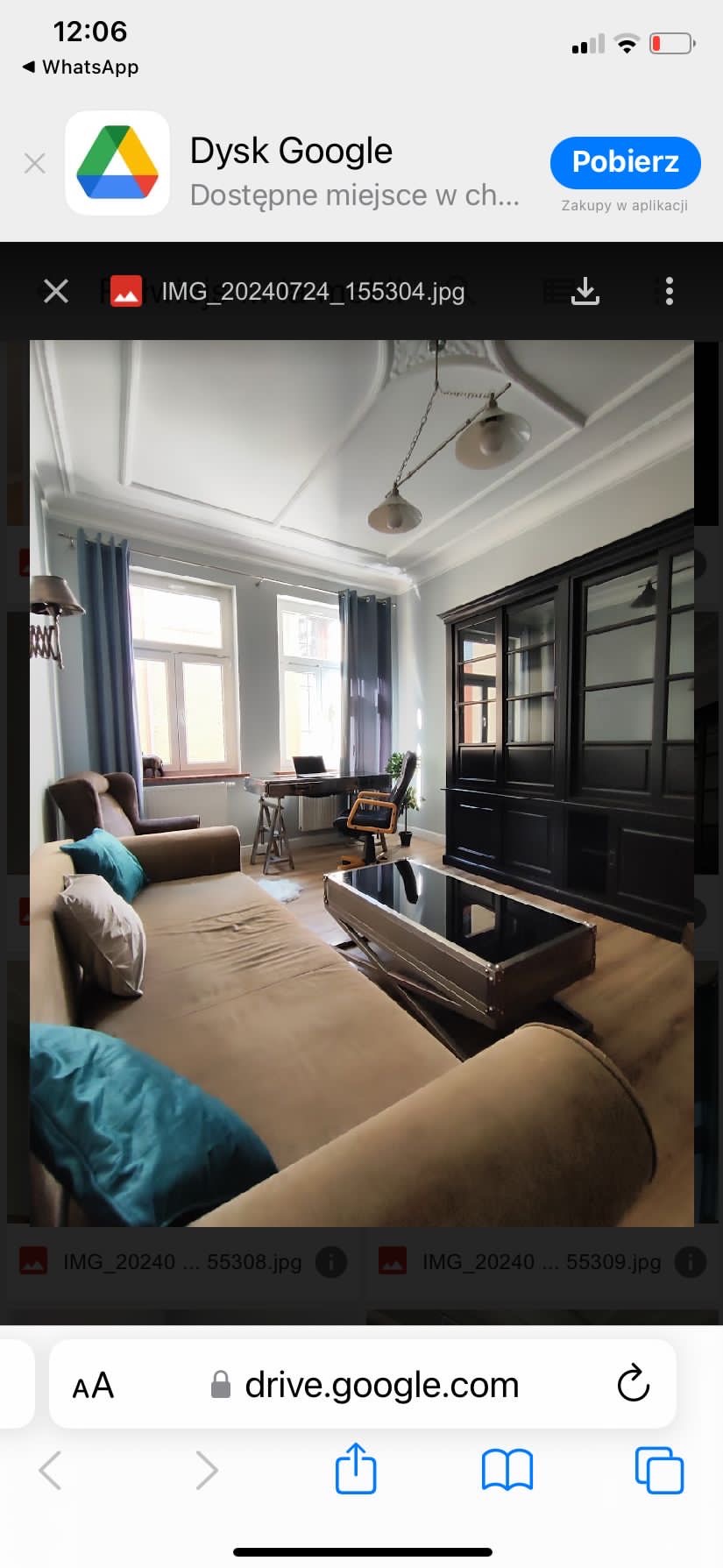 Jasne wnętrze pokoju dziennego z beżową sofą, czarną witryną, biurkiem z komputerem pod oknem i lampą wiszącą w stylu retro.