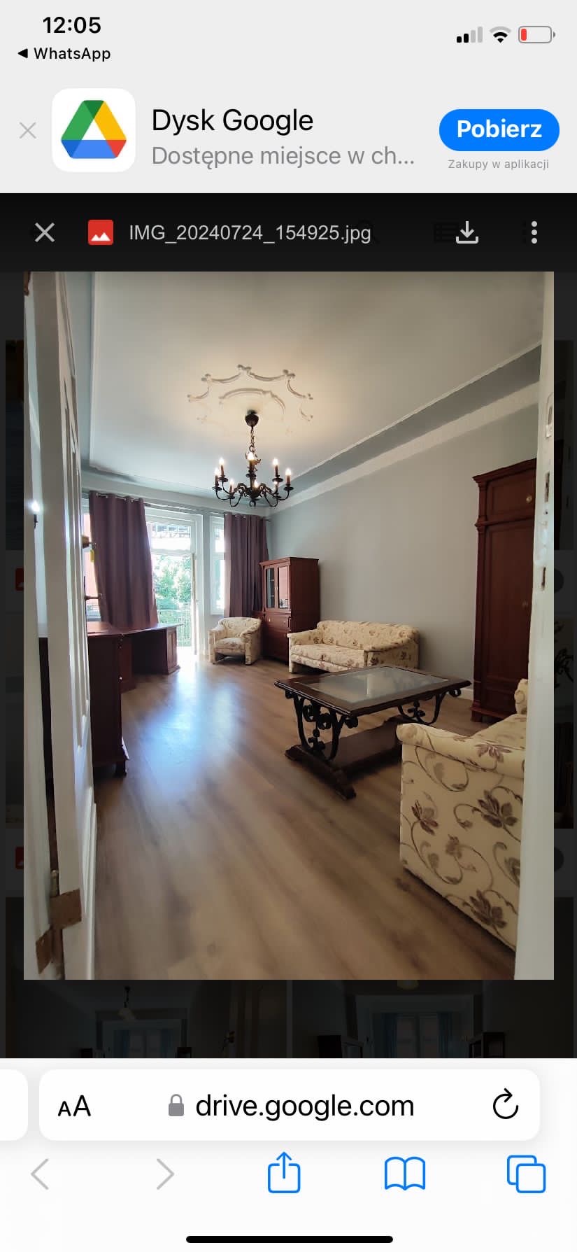 Salon po remoncie z drewnianą podłogą, szarymi ścianami, klasycznymi meblami i ozdobnym żyrandolem, widok zza otwartych drzwi.