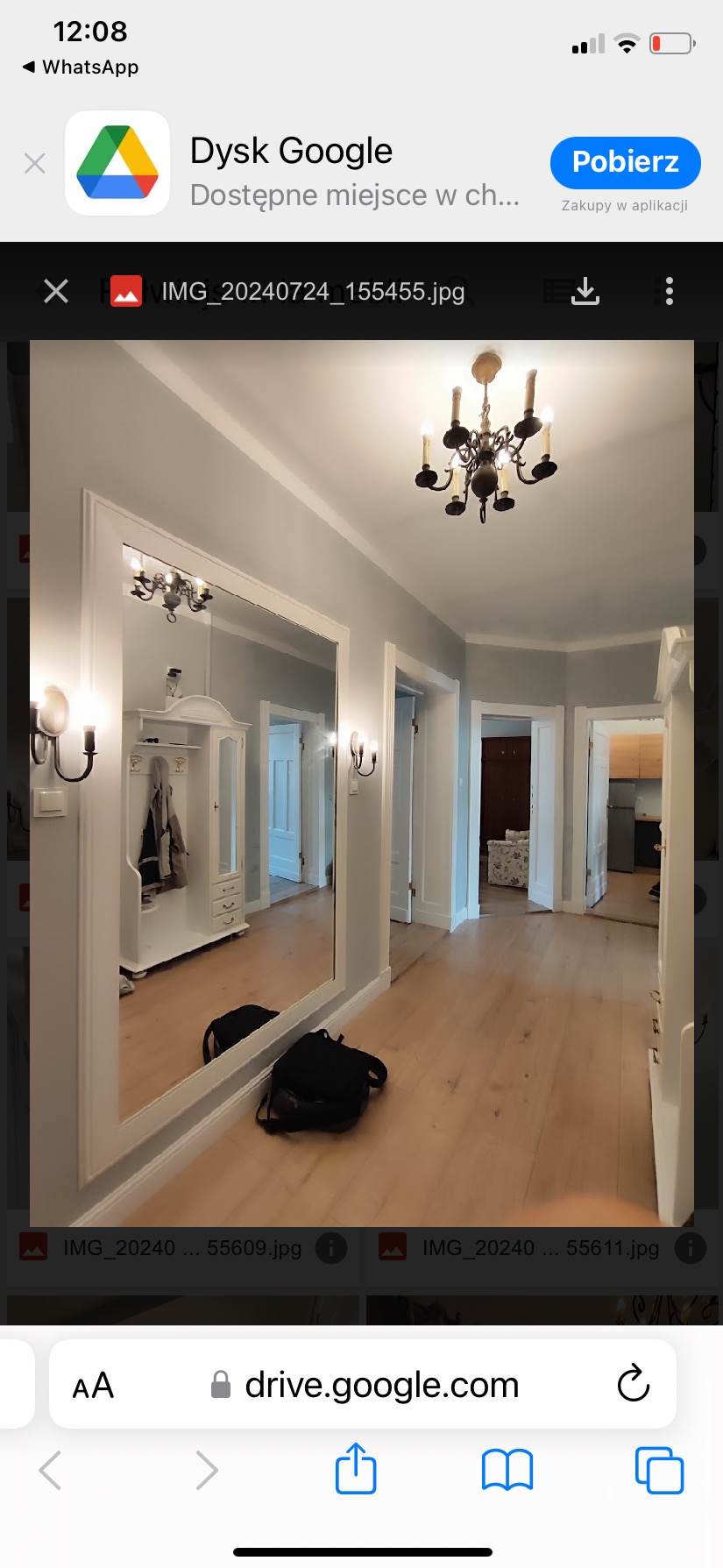 Korytarz po remoncie z drewnianą podłogą, dużym lustrem w białej ramie i ozdobnym żyrandolem, widoczne drzwi do innych pomieszczeń.