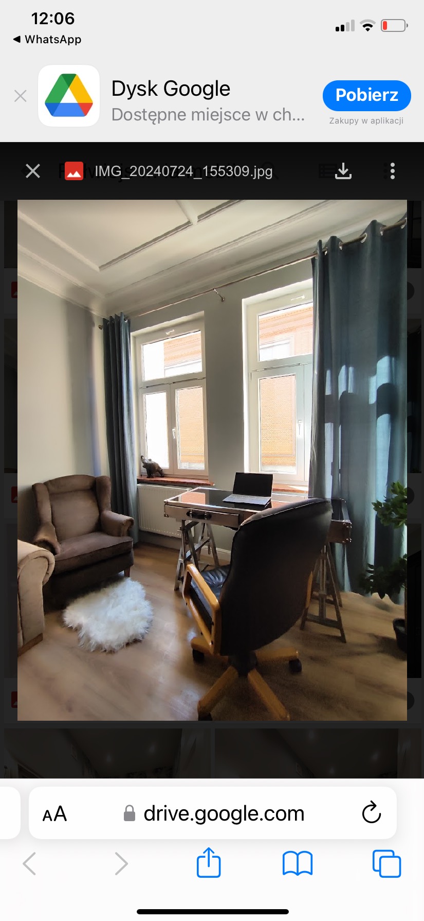 Jasny pokój z dwoma oknami i szarymi ścianami, z biurkiem, laptopem i krzesłem biurowym, uzupełniony o fotel i dywanik.