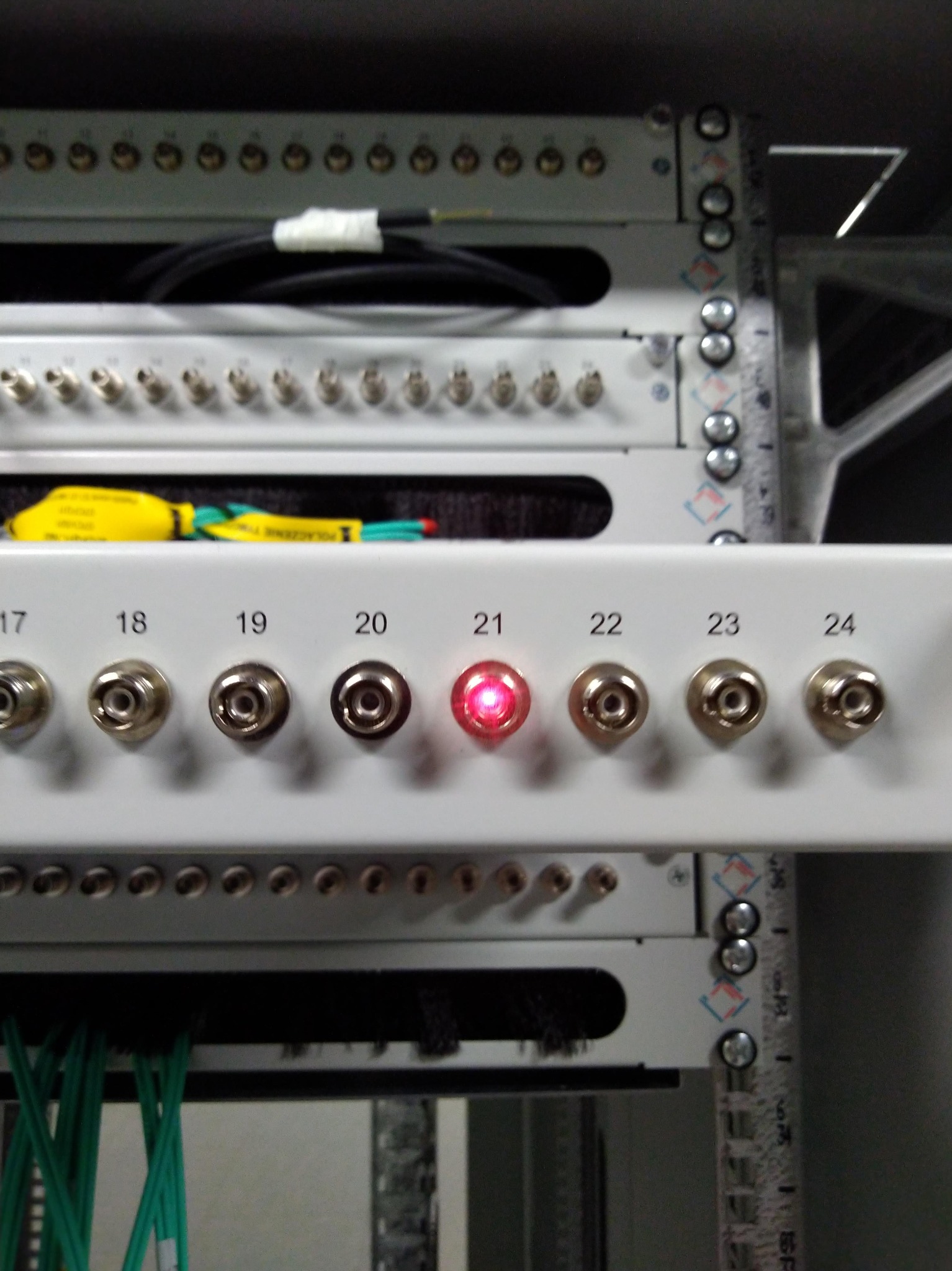 Panel krosowniczy z portami oznaczonymi numerami, z których jeden świeci na czerwono, widoczne kable i elementy szafy rack.