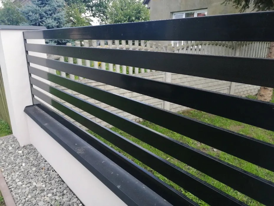 Nowoczesne, poziome przęsła w kolorze antracytowym, zamontowane na białym, niskim murku z podmurówką, widok z zewnątrz posesji.