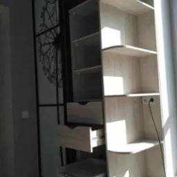 Jasna szafa z przesuwnymi drzwiami z motywem dmuchawca, widoczne otwarte szuflady i półki, oświetlone promieniami słonecznymi