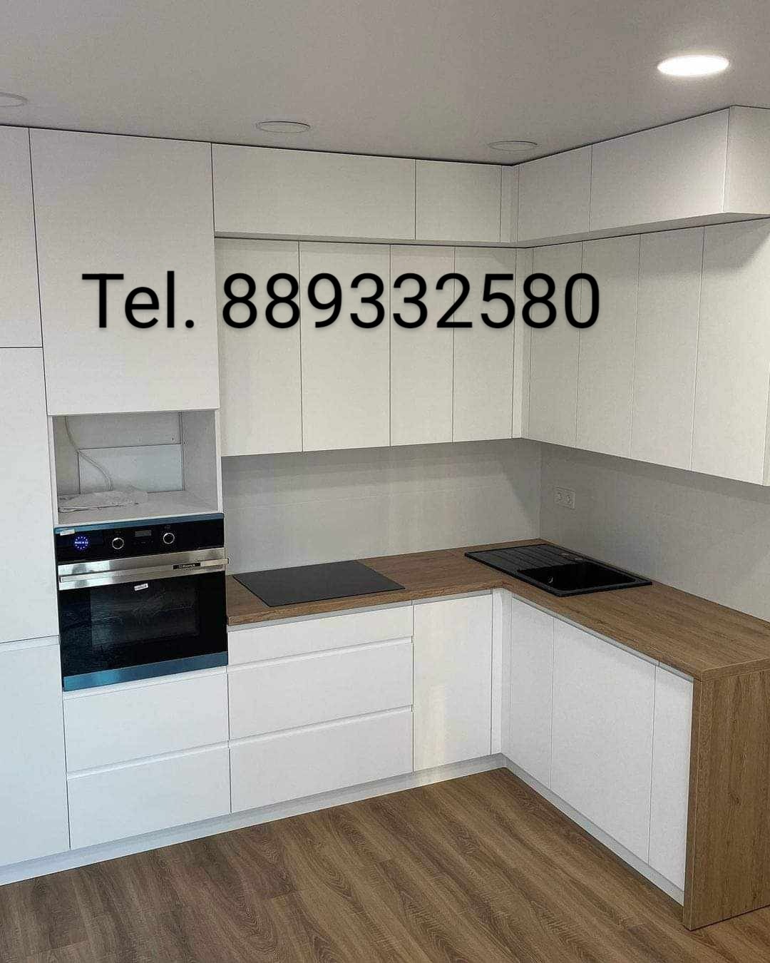 Nowoczesna kuchnia na wymiar z białymi frontami i drewnianym blatem, widoczny piekarnik z niebieską folią ochronną i czarny zlew w rogu.