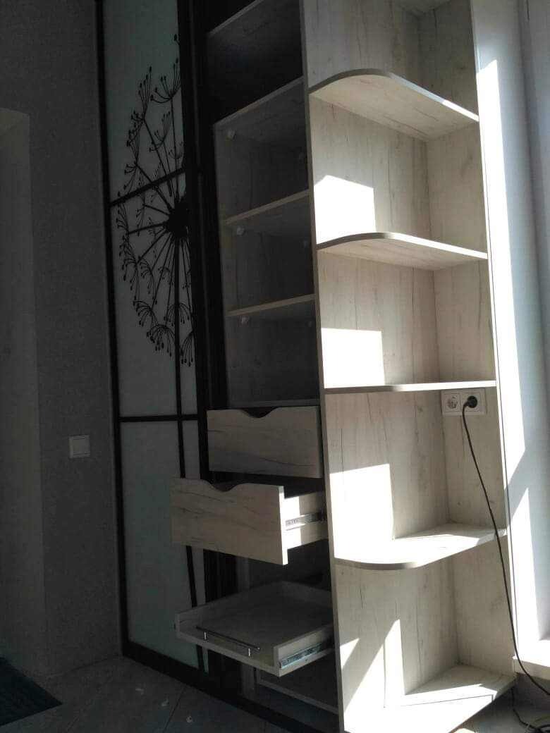 Jasna szafa z przesuwnymi drzwiami z motywem dmuchawca, widoczne otwarte szuflady i półki, oświetlone promieniami słonecznymi