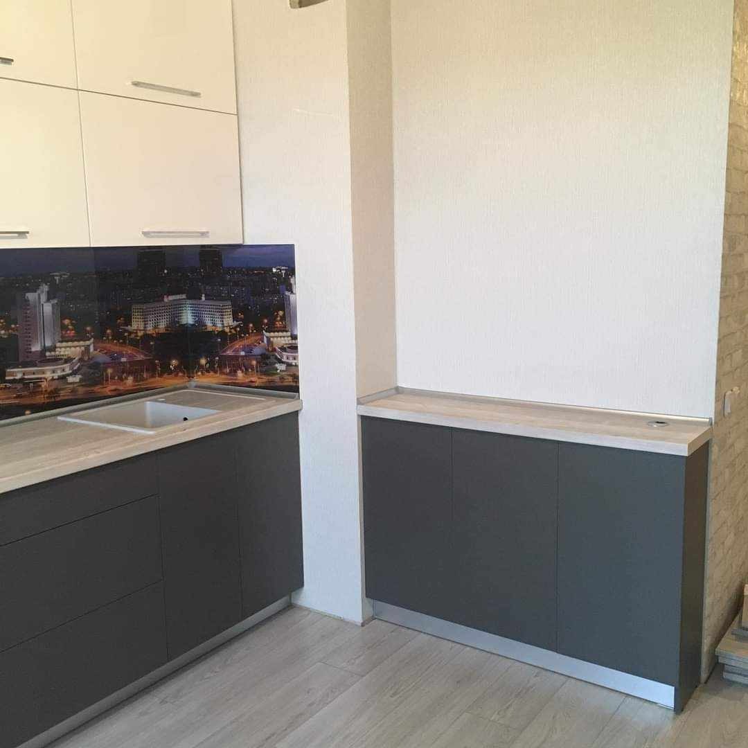 Fragment nowoczesnej kuchni z szarymi szafkami dolnymi, jasnym blatem i fototapetą z nocnym widokiem miasta nad zlewem.