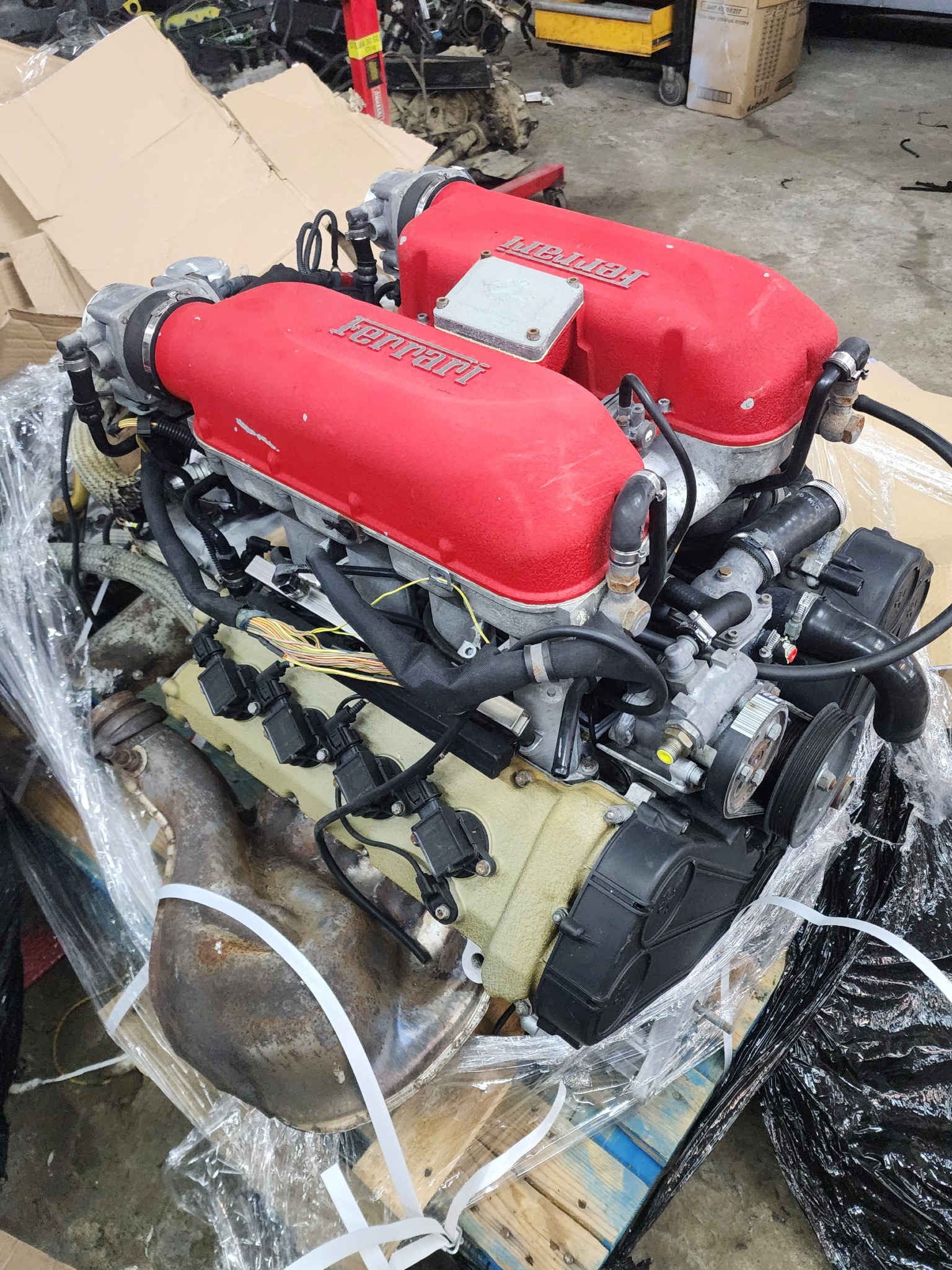 Używany silnik Ferrari z czerwonymi pokrywami zaworów, widoczny na palecie w warsztacie w Korczynie, przygotowany do transportu z owiniętą folią i taśmą.