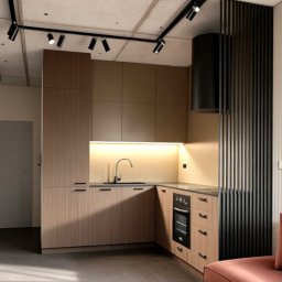 BK Design Barbara Kubica - Nowoczesna kuchnia z drewnianymi frontami, czarnym okapem i oświetleniem punktowym. Minimalistyczny design z elementami dekoracyjnymi, jak lampa ścienna.