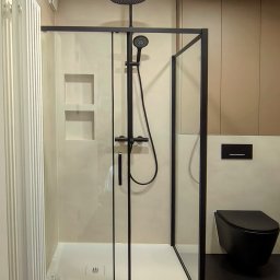 BK Design Barbara Kubica - Nowoczesna kabina prysznicowa z czarną armaturą i odpływem liniowym, minimalistyczna toaleta w kolorze czarnym, beżowe ściany i podłoga w ciemnym kolorze.