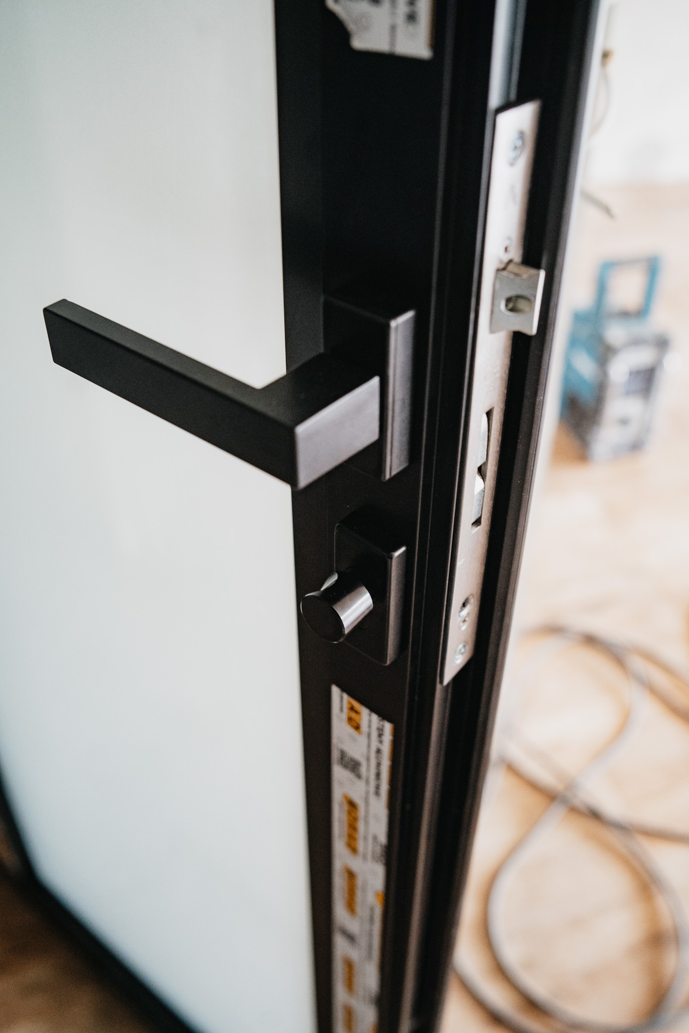 Detal czarnej klamki i zamka w nowo zamontowanych drzwiach z widocznymi elementami montażowymi i narzędziami w tle.