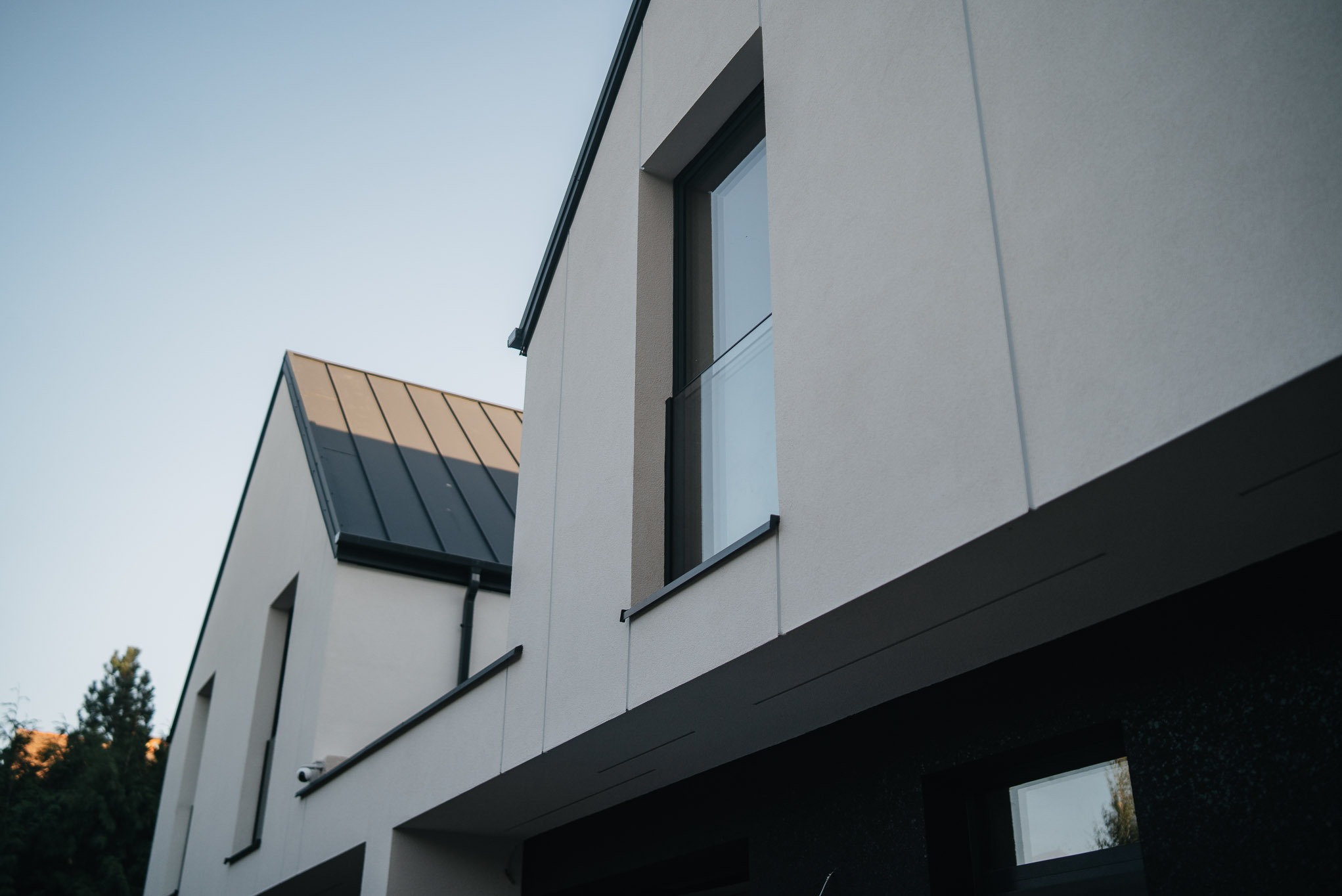 Nowoczesna fasada budynku z oknami w ciemnych ramach, minimalistyczny design i jasna elewacja. Widok z dołu podkreśla geometrię i detale architektoniczne.