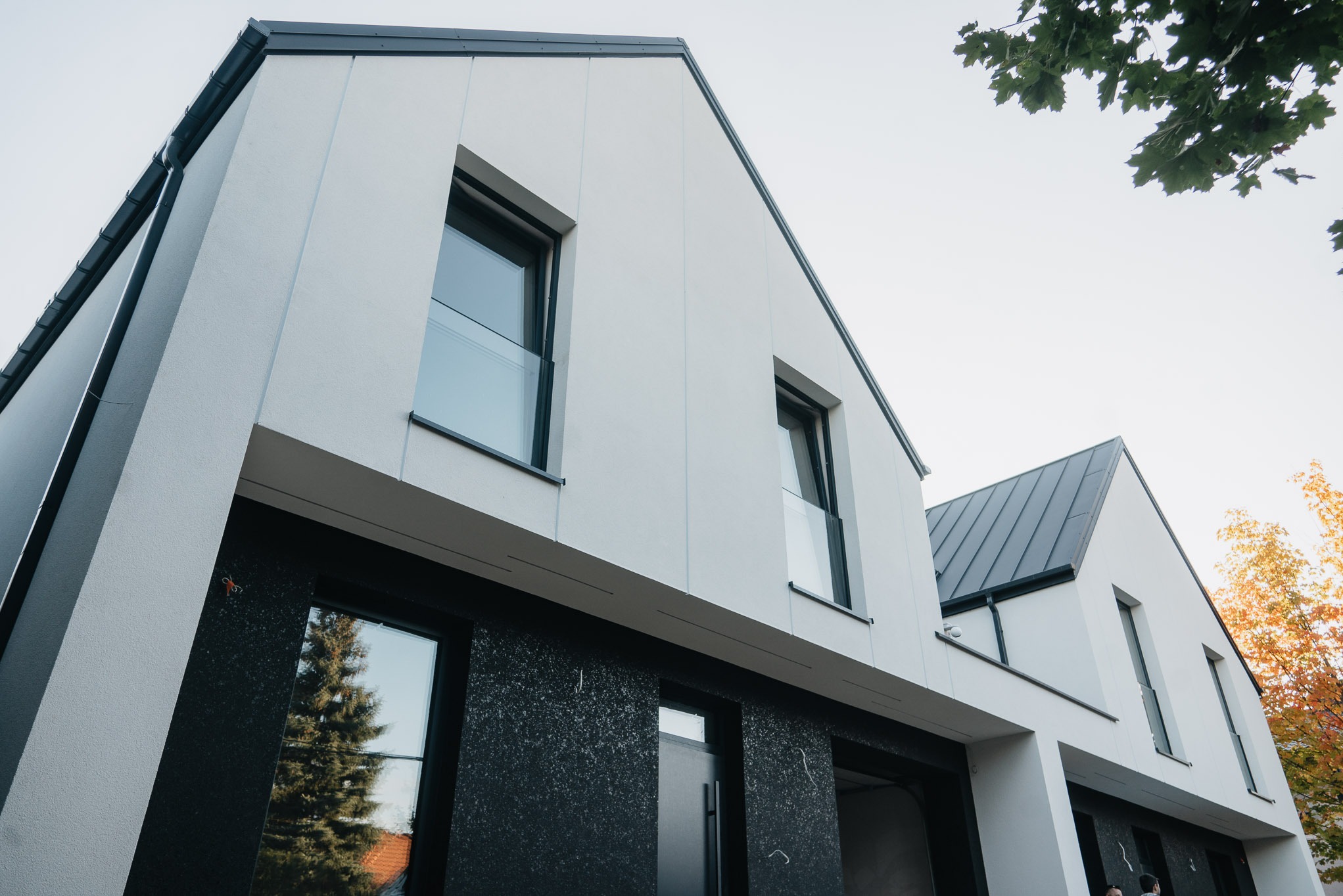 Nowoczesny dom z białymi ścianami i czarnymi akcentami, widok z dołu. Uwagę przyciągają duże okna z balustradami i minimalistyczne wykończenie elewacji.