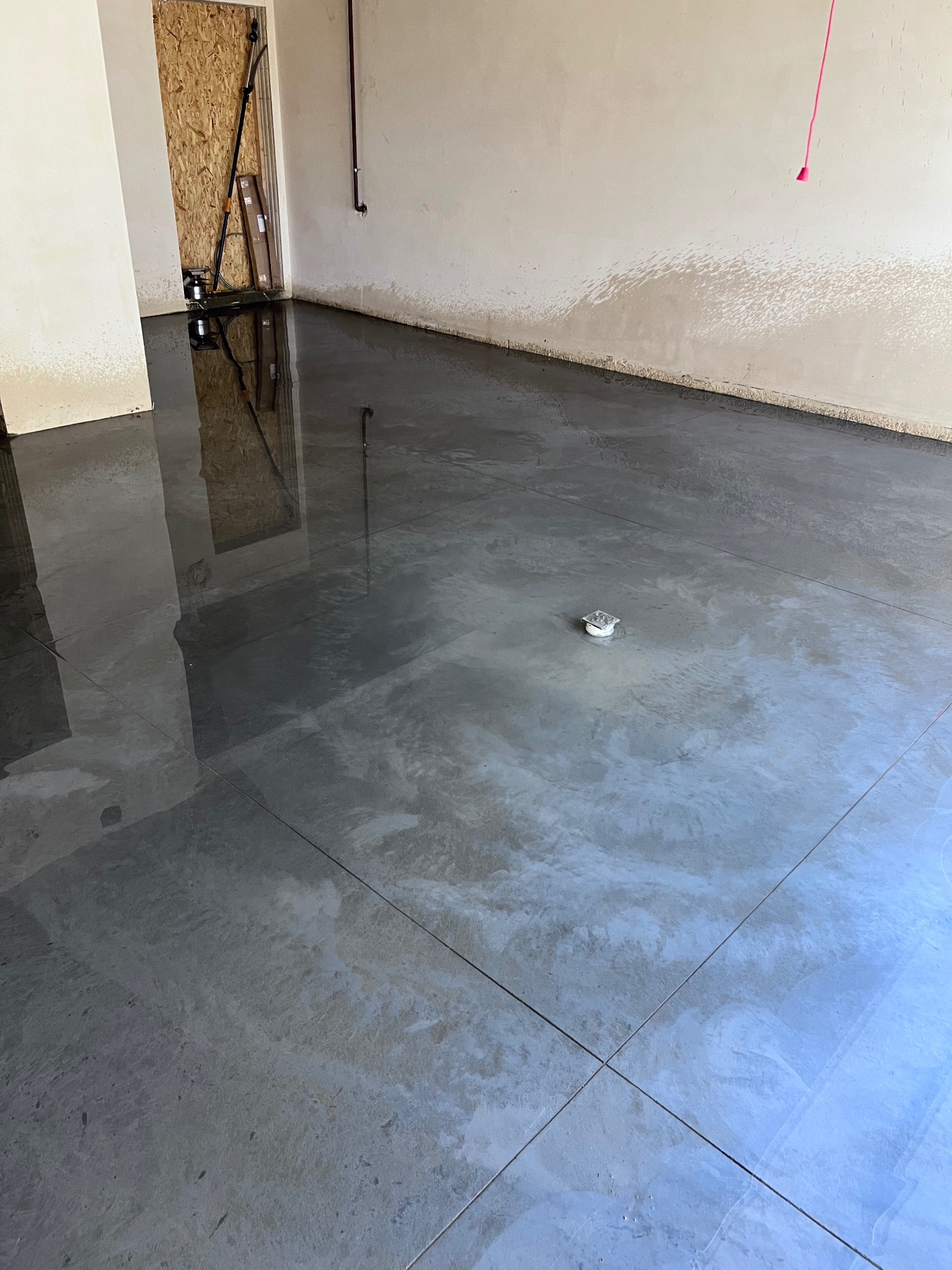 Wypoziomowana, szara posadzka przemysłowa z widocznym odpływem podłogowym i odbiciem narzędzi w tle.