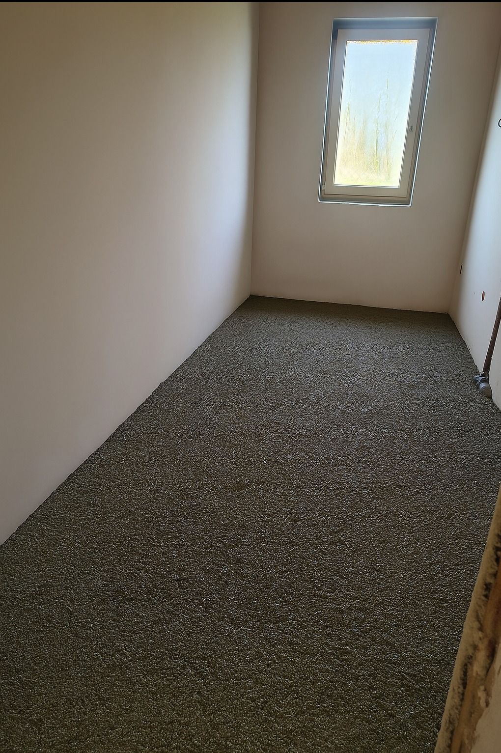 Świeżo wylana, mokra posadzka jastrychowa w jasnym pomieszczeniu z oknem dachowym. Widoczna struktura jastrychu i gładkie, jasne ściany. Ujęcie z narożnika pokoju.