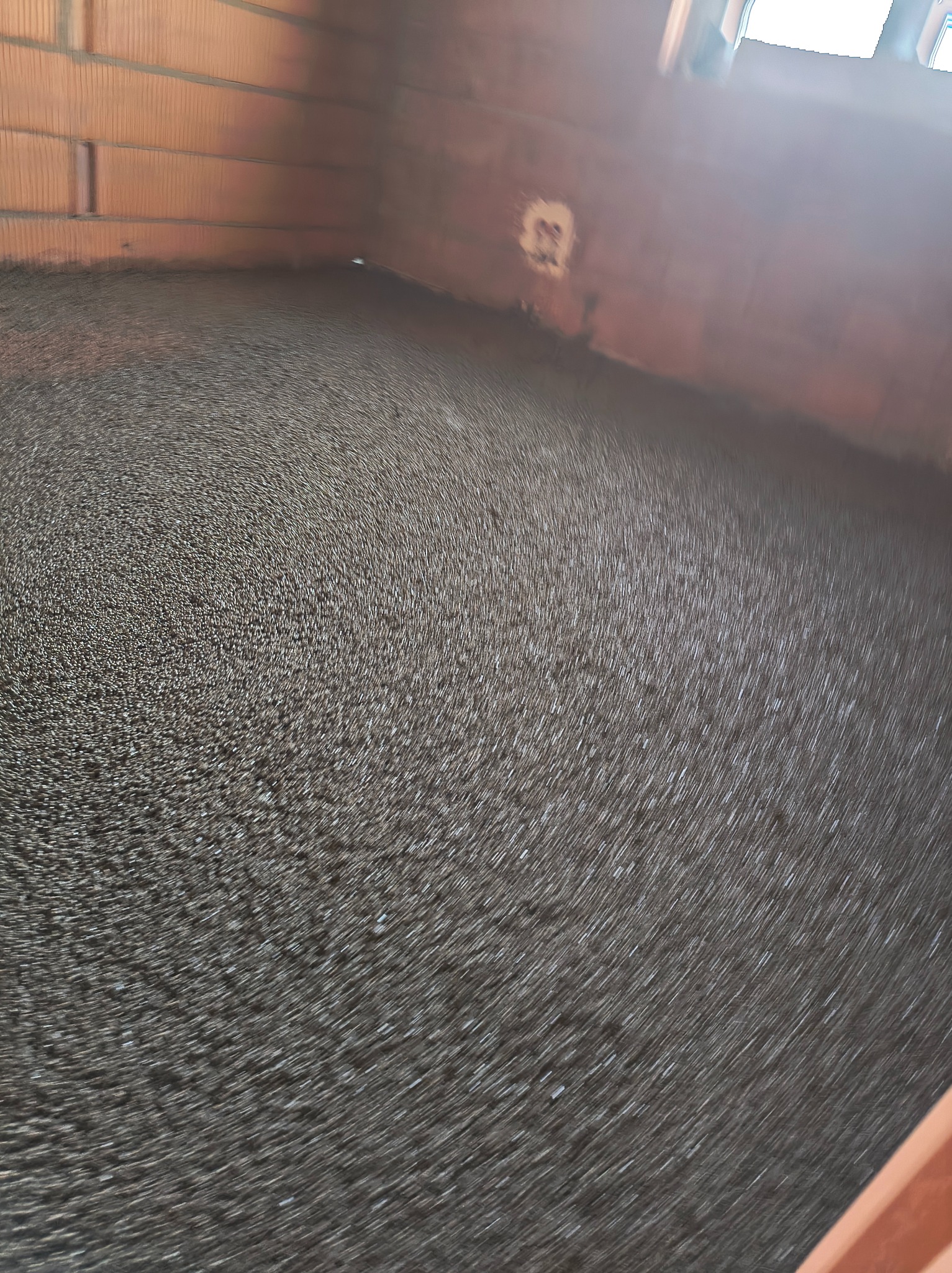 Świeżo wylana, szara posadzka jastrychowa w surowym wnętrzu z ceglanymi ścianami. Widoczne ślady po rozprowadzaniu masy. Ujęcie z niskiego kąta.