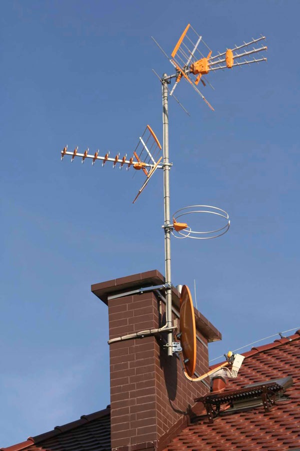 Komplet anten różnego typu (Yagi, paraboliczna, pętlowa) zamontowany na kominie z cegły klinkierowej, widok z dołu na błękitne niebo.
