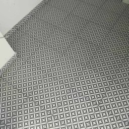 BEE REMONT ANIS DJEBAILI - Nowo ułożona podłoga z płytek ceramicznych w geometryczny wzór czarno-białych kwiatów, widoczna przy białej ścianie w rogu pomieszczenia.