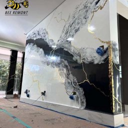 BEE REMONT ANIS DJEBAILI - Ściana z efektem marmuru w odcieniach bieli, szarości i czerni z żyłkami złota, widoczne zabezpieczone gniazdka elektryczne i fragment podłogi w trakcie prac wykończeniowych.