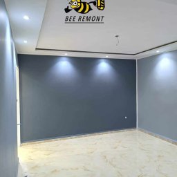 BEE REMONT ANIS DJEBAILI - Wnętrze pokoju po malowaniu ścian na ciemny szary kolor w Pile, widoczna marmurkowa podłoga i logo firmy malarskiej na suficie.