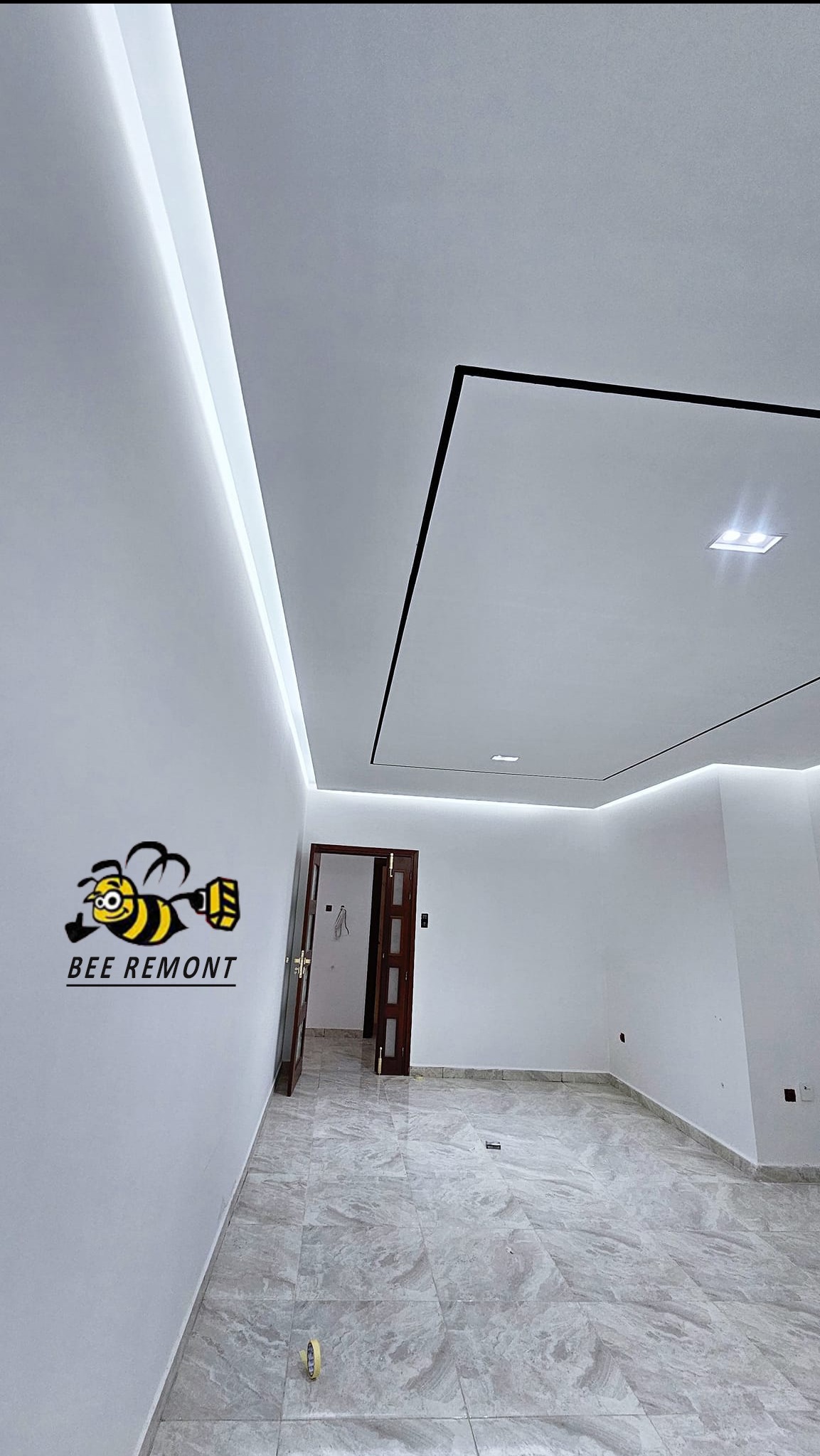 Wykończone wnętrze: białe ściany, marmurowe płytki podłogowe, sufit z oświetleniem LED i czarnymi listwami dekoracyjnymi, otwarte drzwi w tle, widoczne logo firmy na ścianie.