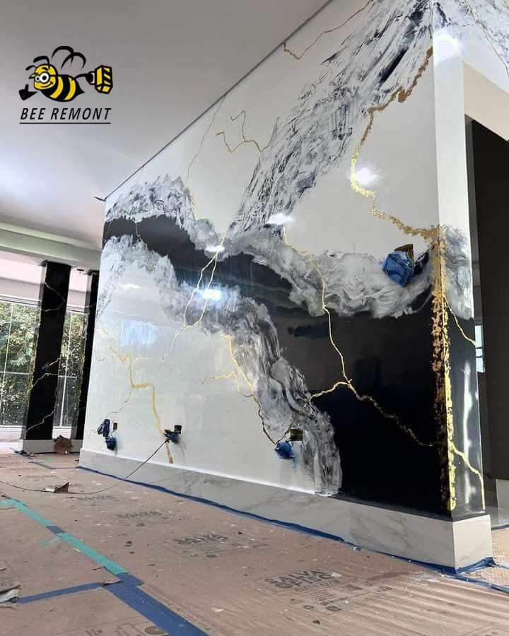 Ściana z efektem marmuru w odcieniach bieli, szarości i czerni z żyłkami złota, widoczne zabezpieczone gniazdka elektryczne i fragment podłogi w trakcie prac wykończeniowych.