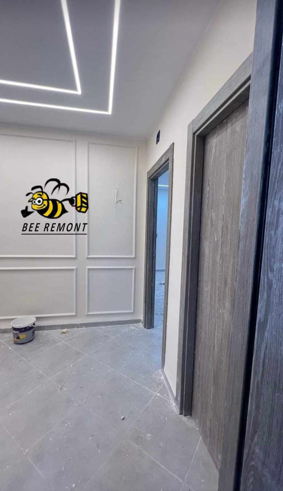 Świeżo wyremontowane wnętrze z dekoracyjnymi panelami ściennymi, podświetleniem LED na suficie i dwiema parami szarych drzwi, na ścianie widoczne logo firmy remontowej.