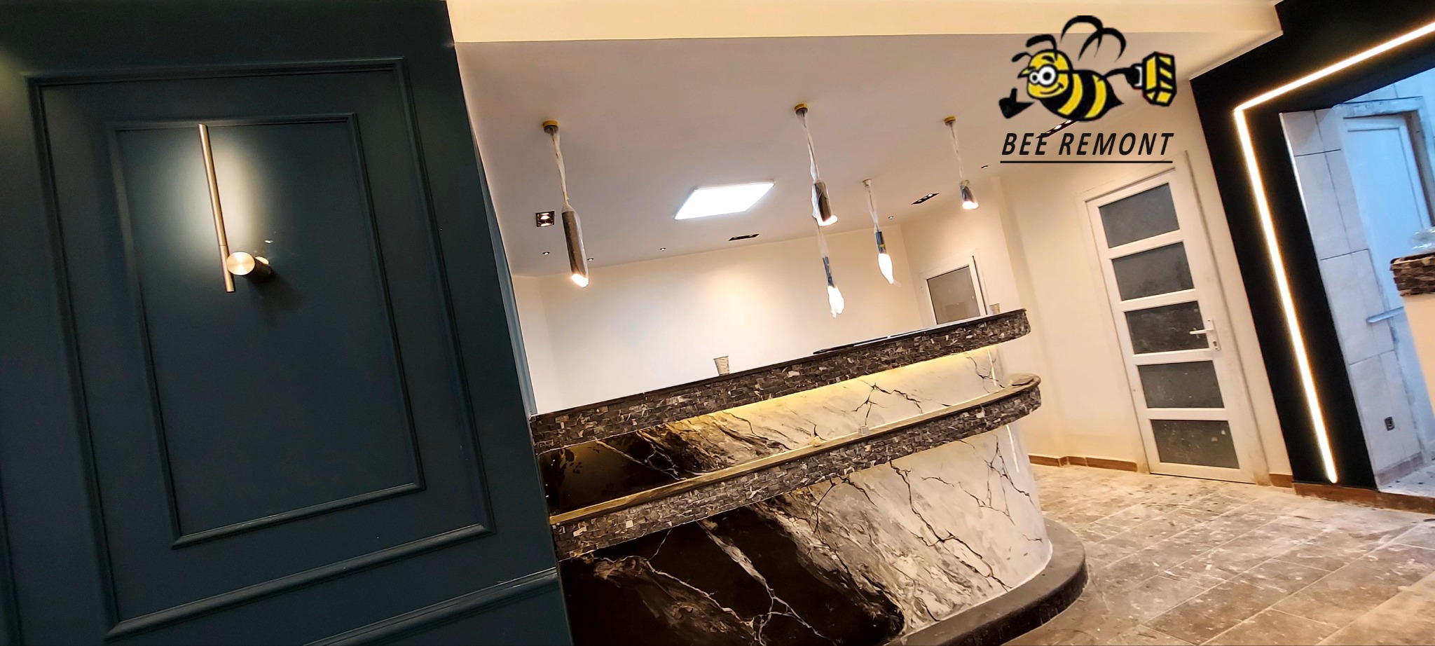 Wykończone wnętrze z recepcją o marmurowym wzorze, oświetleniem punktowym i dekoracyjnym panelem ściennym w kolorze butelkowej zieleni, widoczne logo firmy remontowej.