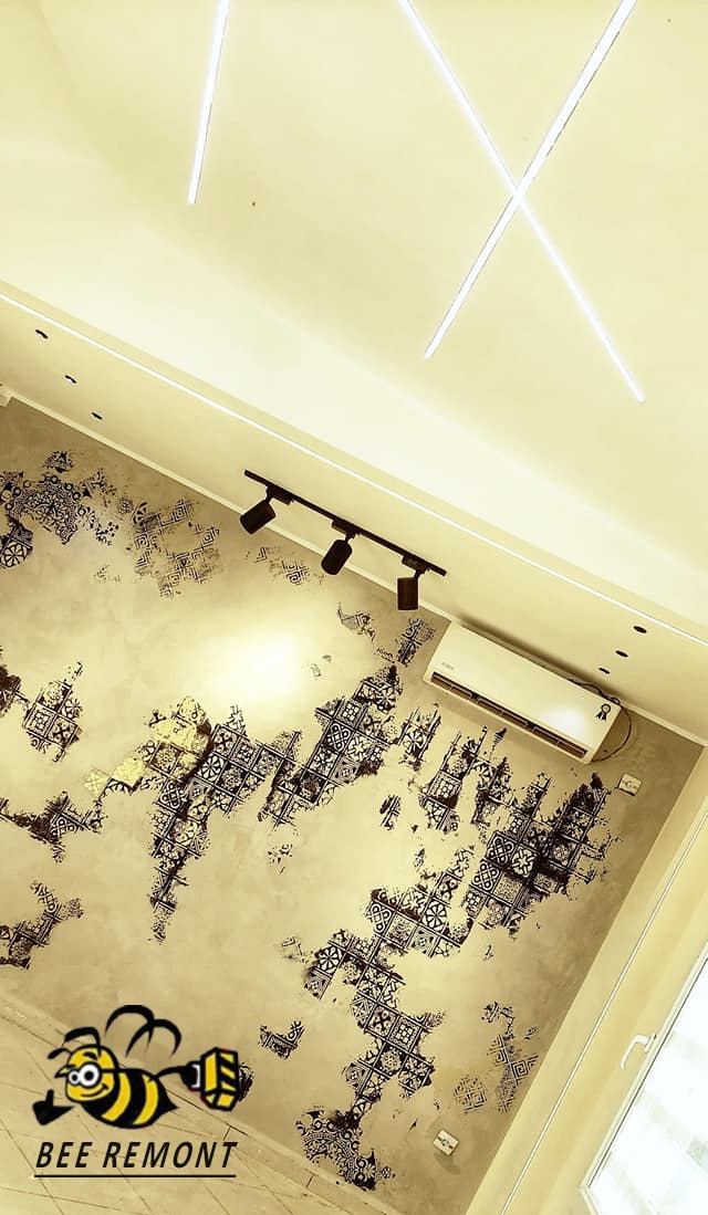 Ściana w pokoju po dekoracyjnym malowaniu z czarnymi wzorami, oświetlona reflektorami i lampami LED na suficie, widoczny klimatyzator i logo firmy 'BEE REMONT'.