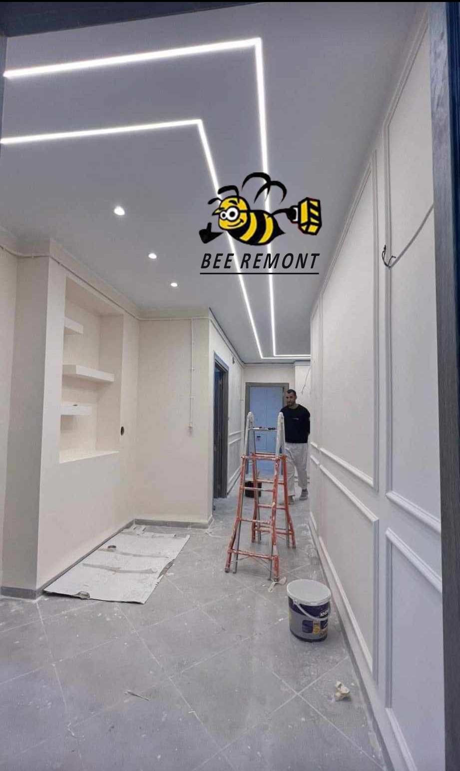 Korytarz w trakcie wykańczania z dekoracyjnymi panelami ściennymi, podświetlanym sufitem i logiem firmy 'BEE REMONT' na suficie, widoczna drabina i osoba w tle.